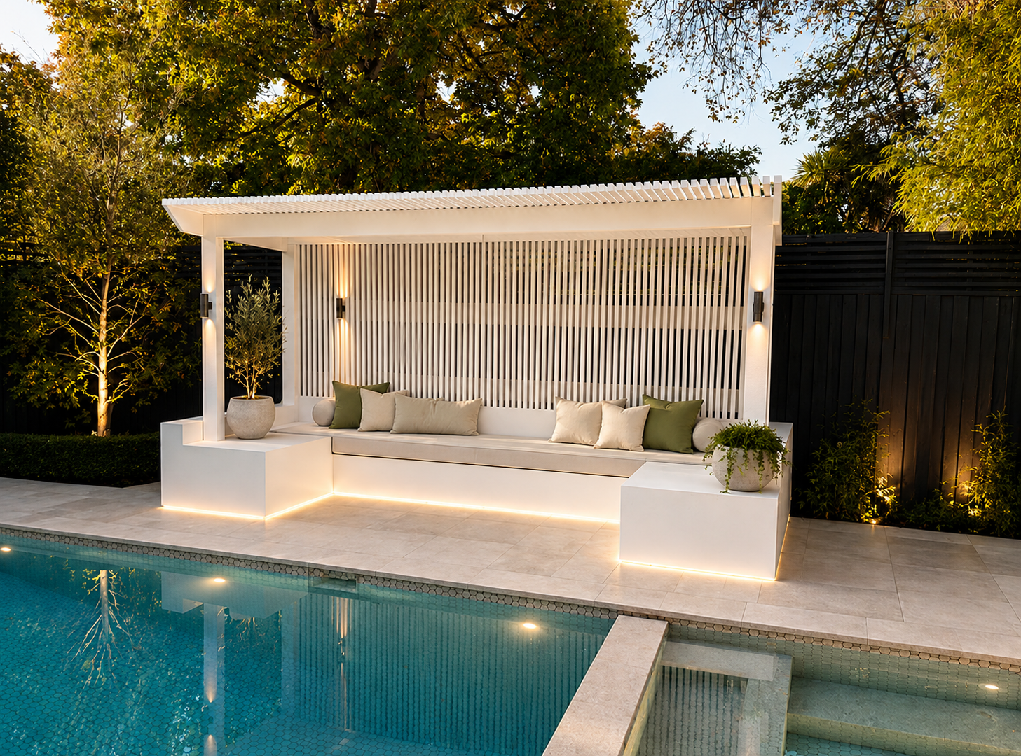 Completed PJR Kew poolside build with white batten pergola, slatted screen, built-in bench, warm lighting and pale paving